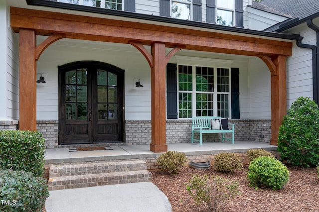 view of exterior entry featuring a porch, brick siding, and french doors