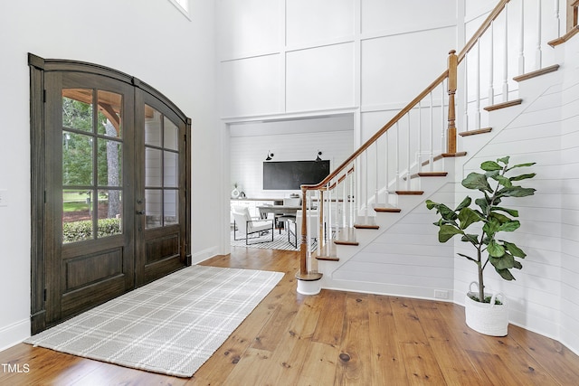 entrance foyer featuring stairway, wood-type flooring, french doors, and a towering ceiling
