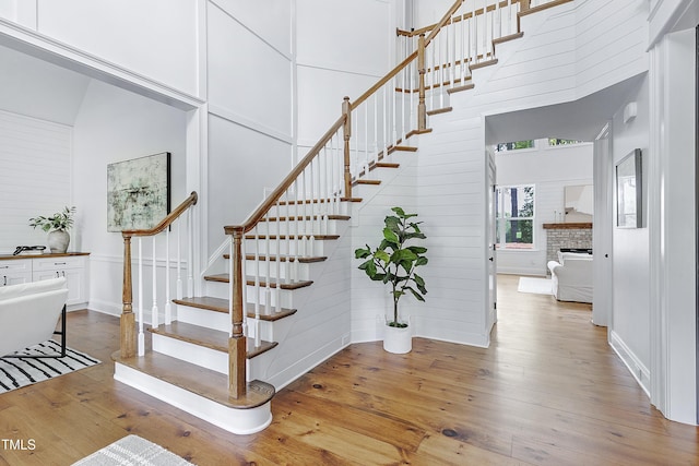 staircase with a fireplace, wood-type flooring, and a towering ceiling