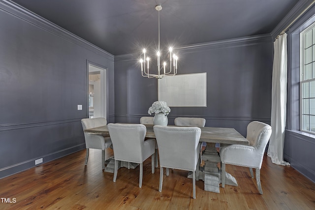 dining area featuring an inviting chandelier, crown molding, a decorative wall, and wood finished floors