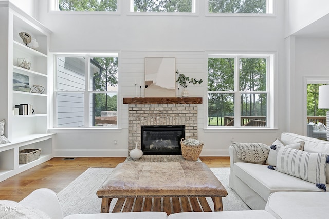 living area featuring baseboards, a high ceiling, a brick fireplace, and wood finished floors
