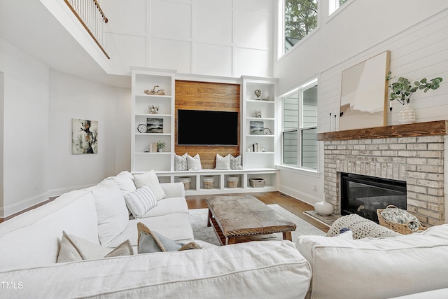 living area with a fireplace, baseboards, wood finished floors, and a towering ceiling