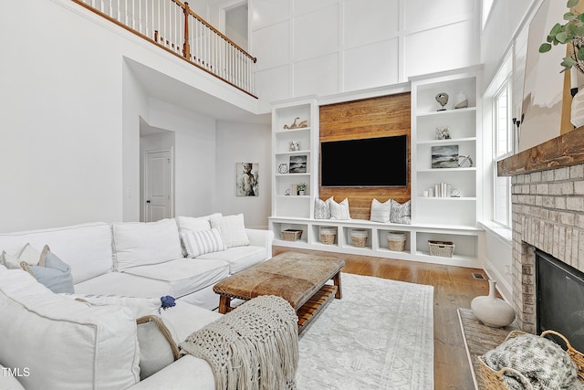 living area with a fireplace, plenty of natural light, wood finished floors, and a towering ceiling