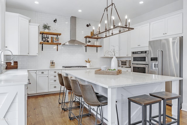 kitchen with wall chimney range hood, open shelves, appliances with stainless steel finishes, and a sink