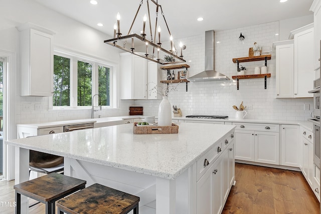 kitchen featuring open shelves, wall chimney range hood, a center island, gas stovetop, and tasteful backsplash