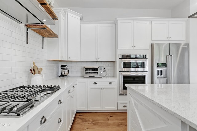 kitchen featuring a toaster, white cabinetry, light wood finished floors, backsplash, and stainless steel appliances