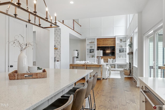 kitchen featuring stainless steel dishwasher, a towering ceiling, wood finished floors, light stone countertops, and a kitchen bar