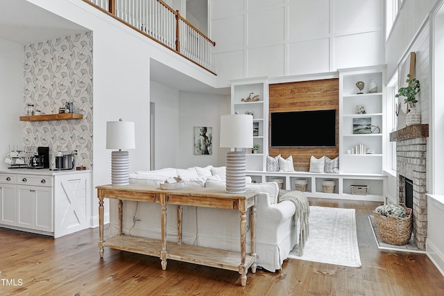 living room featuring a towering ceiling, a fireplace, built in shelves, wood finished floors, and baseboards