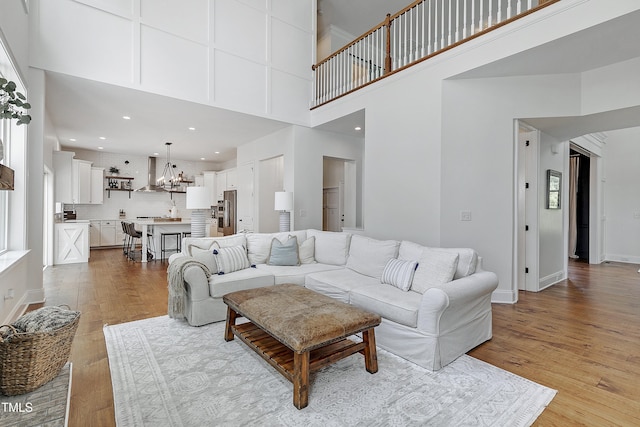 living area with baseboards, a notable chandelier, wood finished floors, and a towering ceiling