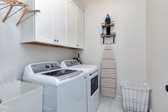 laundry area with independent washer and dryer, cabinet space, a sink, baseboards, and light tile patterned flooring