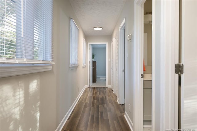 hall with baseboards, a textured ceiling, and dark wood finished floors