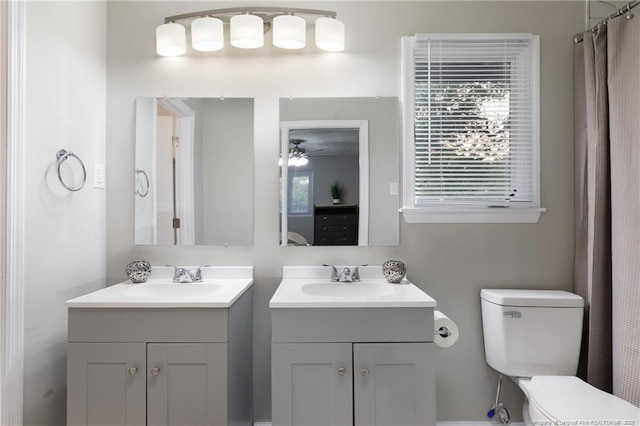 full bath with a sink, ceiling fan, two vanities, and toilet