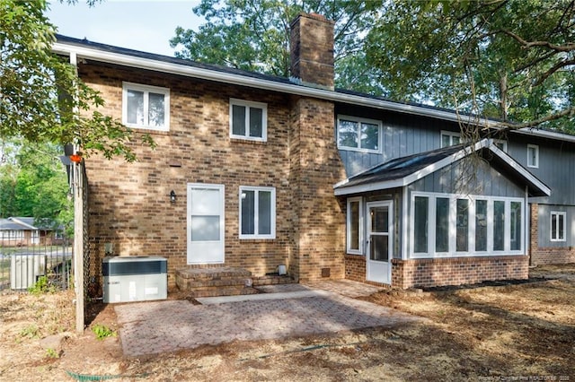 rear view of property with a chimney, a sunroom, central air condition unit, brick siding, and a patio