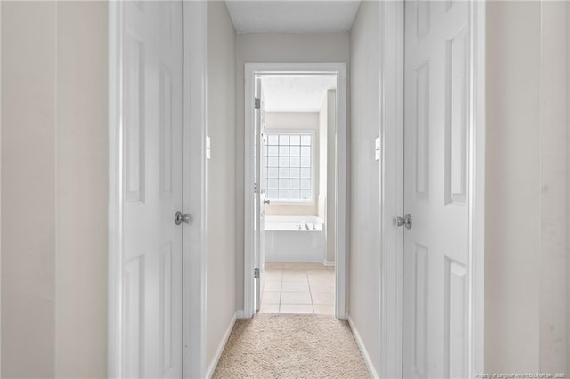 corridor featuring light tile patterned flooring, baseboards, and light colored carpet