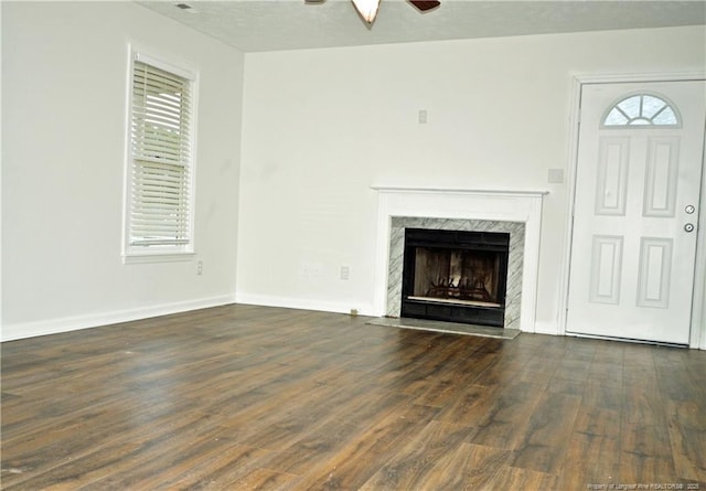 unfurnished living room featuring a healthy amount of sunlight, a high end fireplace, a ceiling fan, and wood finished floors