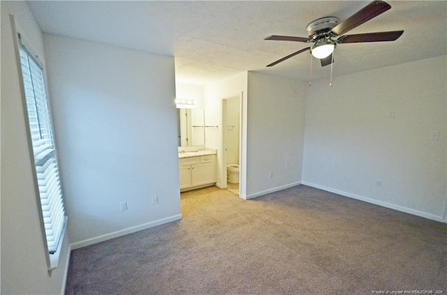 unfurnished bedroom featuring light colored carpet, connected bathroom, baseboards, and ceiling fan