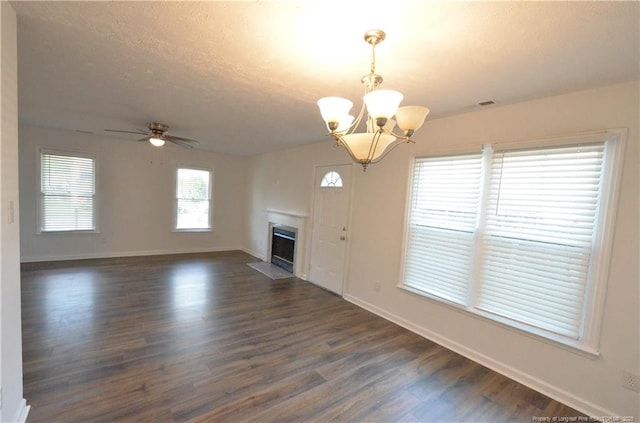 unfurnished living room with dark wood-style flooring, a textured ceiling, a fireplace with flush hearth, baseboards, and ceiling fan with notable chandelier