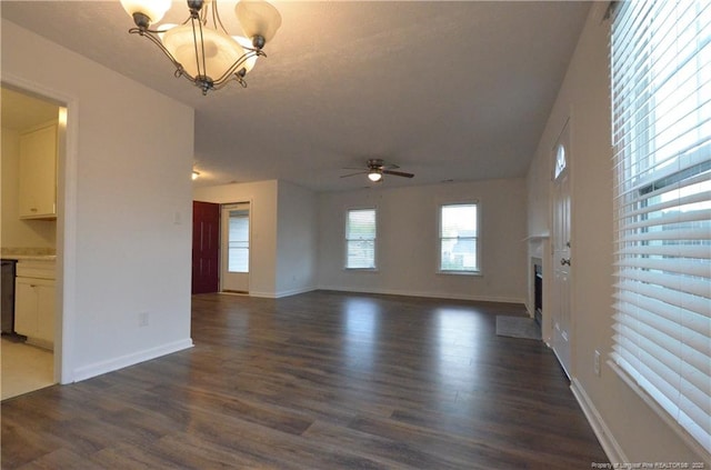unfurnished living room featuring baseboards, a fireplace with raised hearth, ceiling fan with notable chandelier, and dark wood-style floors