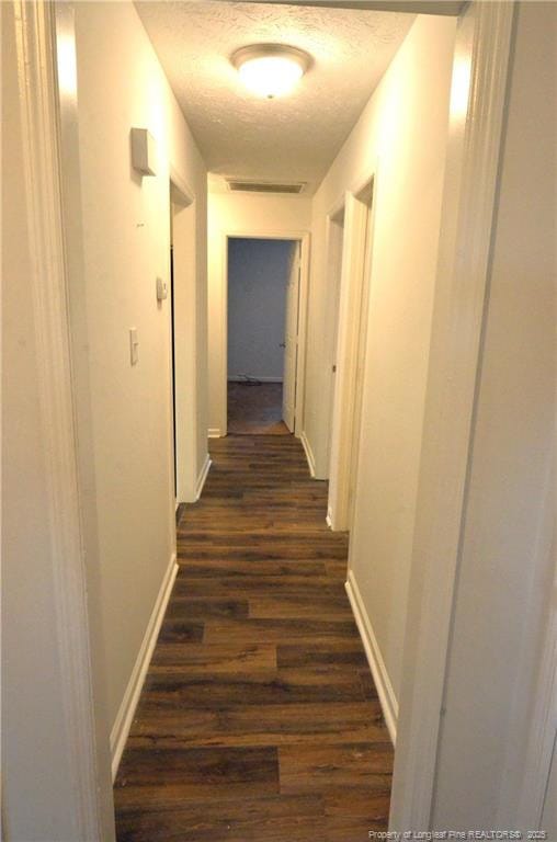 hall with baseboards, dark wood-style flooring, a textured ceiling, and visible vents