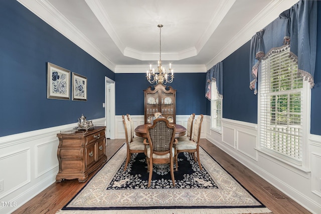 dining room featuring a raised ceiling, wood finished floors, a chandelier, and wainscoting