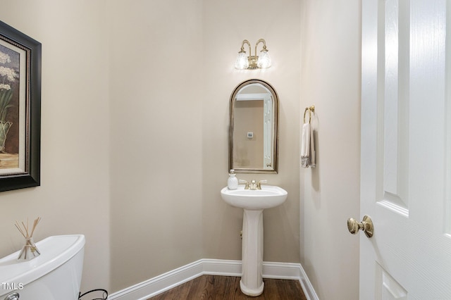 bathroom featuring baseboards, wood finished floors, and toilet