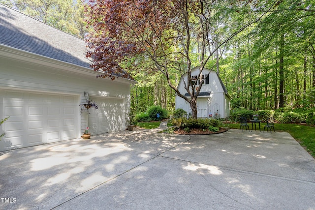 view of side of property with driveway, a shingled roof, an outdoor structure, and a garage