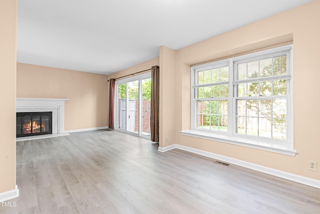 unfurnished living room featuring baseboards, visible vents, a glass covered fireplace, and wood finished floors