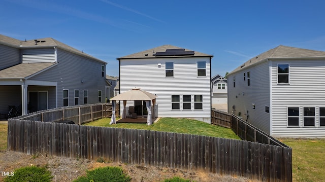rear view of house featuring a lawn, a patio, a fenced backyard, roof mounted solar panels, and a gazebo