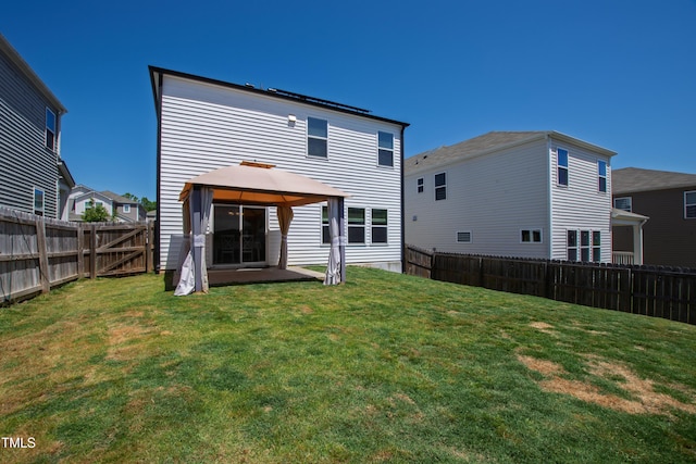 rear view of house featuring a gazebo, a fenced backyard, and a lawn