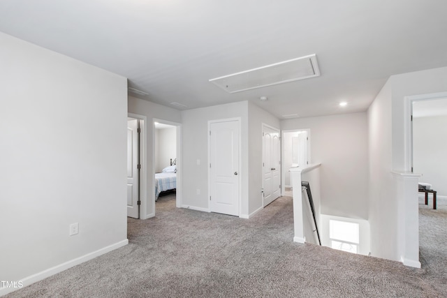 carpeted spare room featuring baseboards and attic access