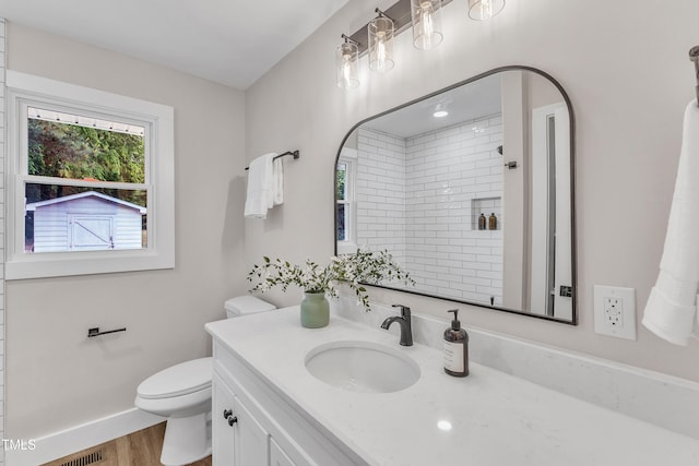 full bath featuring vanity, toilet, baseboards, wood finished floors, and tiled shower