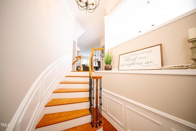 stairway with a wainscoted wall, wood finished floors, and a decorative wall