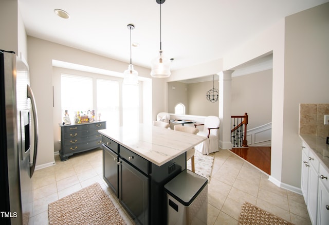 kitchen featuring a kitchen island, hanging light fixtures, light tile patterned floors, baseboards, and stainless steel fridge
