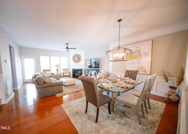 dining room featuring a glass covered fireplace, wood finished floors, and ceiling fan with notable chandelier