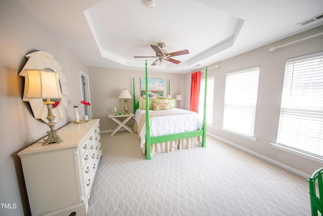 bedroom with visible vents, baseboards, a tray ceiling, and light carpet