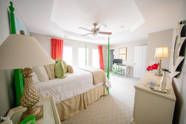 bedroom with baseboards, ceiling fan, a tray ceiling, and light colored carpet
