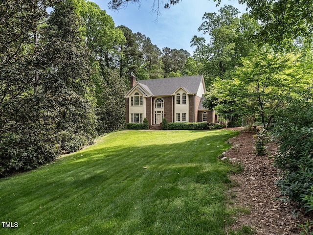 colonial inspired home with brick siding, a front lawn, and a chimney
