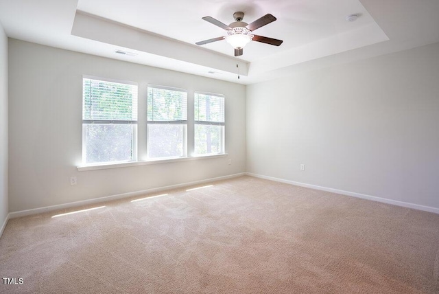 spare room featuring ceiling fan, light colored carpet, baseboards, and a raised ceiling