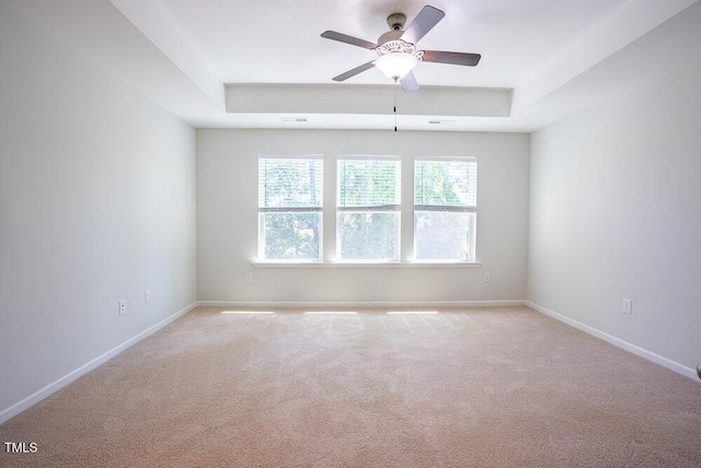 unfurnished room featuring light colored carpet, a ceiling fan, baseboards, and a tray ceiling