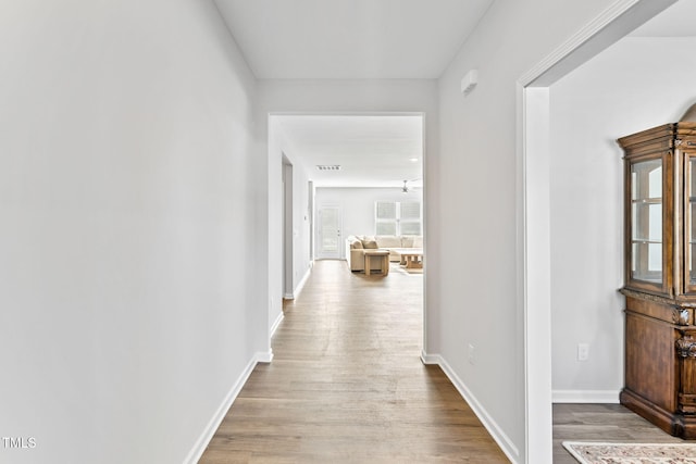 corridor with baseboards, visible vents, and wood finished floors