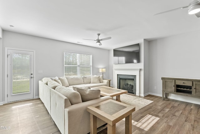 living room featuring a fireplace, light wood-style flooring, baseboards, and a ceiling fan