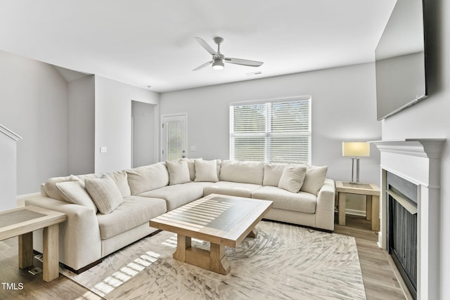 living area featuring a fireplace, visible vents, baseboards, ceiling fan, and light wood-style floors