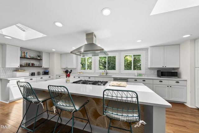 kitchen with a breakfast bar, island range hood, backsplash, a skylight, and stainless steel appliances