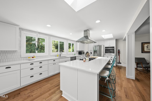 kitchen featuring a kitchen breakfast bar, island exhaust hood, a sink, a skylight, and stainless steel appliances