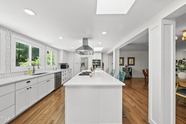 kitchen with range hood, white cabinets, a sink, appliances with stainless steel finishes, and a skylight