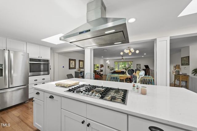 kitchen featuring white cabinets, appliances with stainless steel finishes, light wood-style flooring, wall chimney exhaust hood, and ornate columns