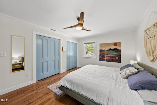 bedroom featuring wood finished floors, ornamental molding, two closets, and visible vents