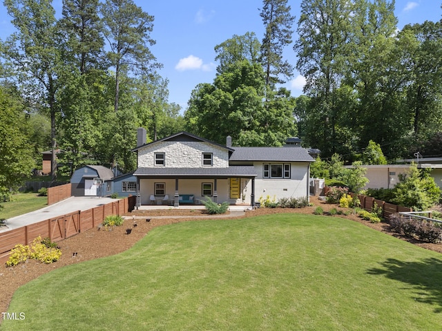 back of house with fence, covered porch, a chimney, concrete driveway, and a yard
