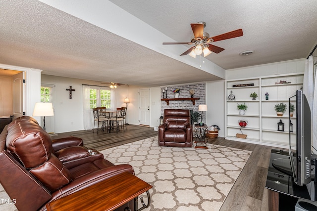 living room with a ceiling fan, a textured ceiling, visible vents, and wood finished floors