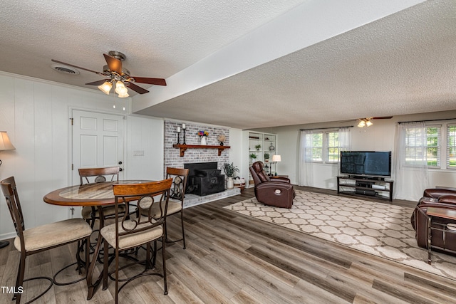 living room featuring a ceiling fan, a textured ceiling, wood finished floors, and a wood stove